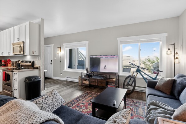 A modern living room with a sofa, coffee table, TV, and a bike in the background.