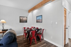 A dining area with a wooden table and red chairs, a lamp, and two framed pictures on the wall.