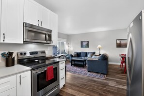 A modern kitchen with white cabinets, stainless steel appliances, and a red towel hanging from the oven handle.