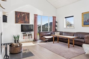 A modern living room with a brown leather sofa, a wooden coffee table, a flat-screen TV, and a bookshelf. - Lovely holiday home near Hasmark Beach (Otterup)