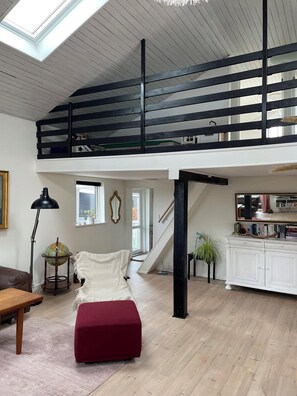 A loft-style room with a high ceiling, a staircase, a red ottoman, a globe on a stand, and a white cabinet. - Lovely holiday home near Hasmark Beach (Otterup)
