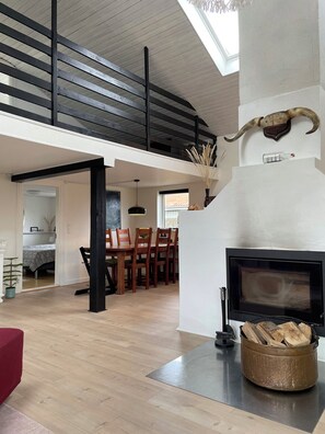 A spacious living area with a high ceiling, a fireplace, wooden flooring, and a dining area with chairs and a table. - Lovely holiday home near Hasmark Beach (Otterup)