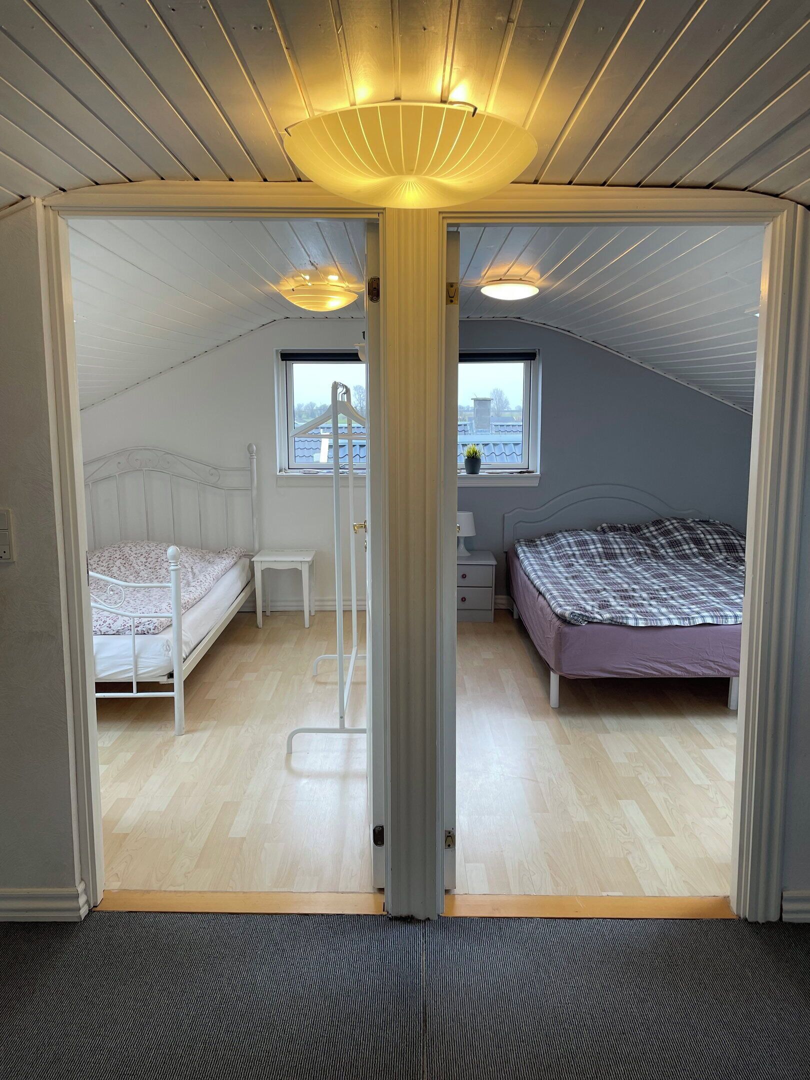 A room with two beds, a window, and a ceiling light fixture.