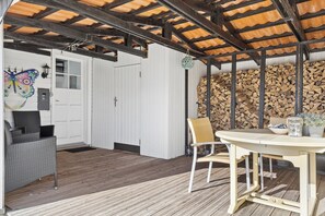 A covered outdoor area with a table and chairs, a white door, and a wall of stacked firewood. - Lovely holiday home near Hasmark Beach (Otterup)