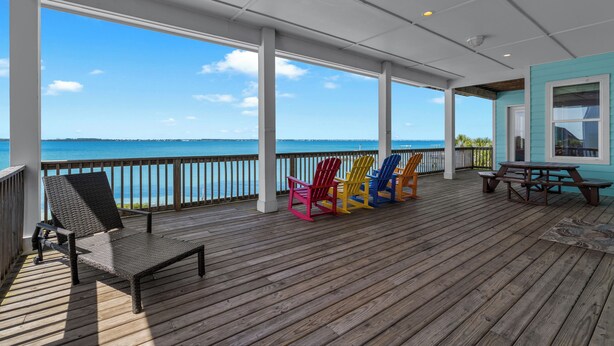A covered deck with a view of the ocean, wooden chairs, and a picnic table. - Baywatch Beach House | Private Pool | Beach Service Included | Dog Friendly (Pensacola Beach)