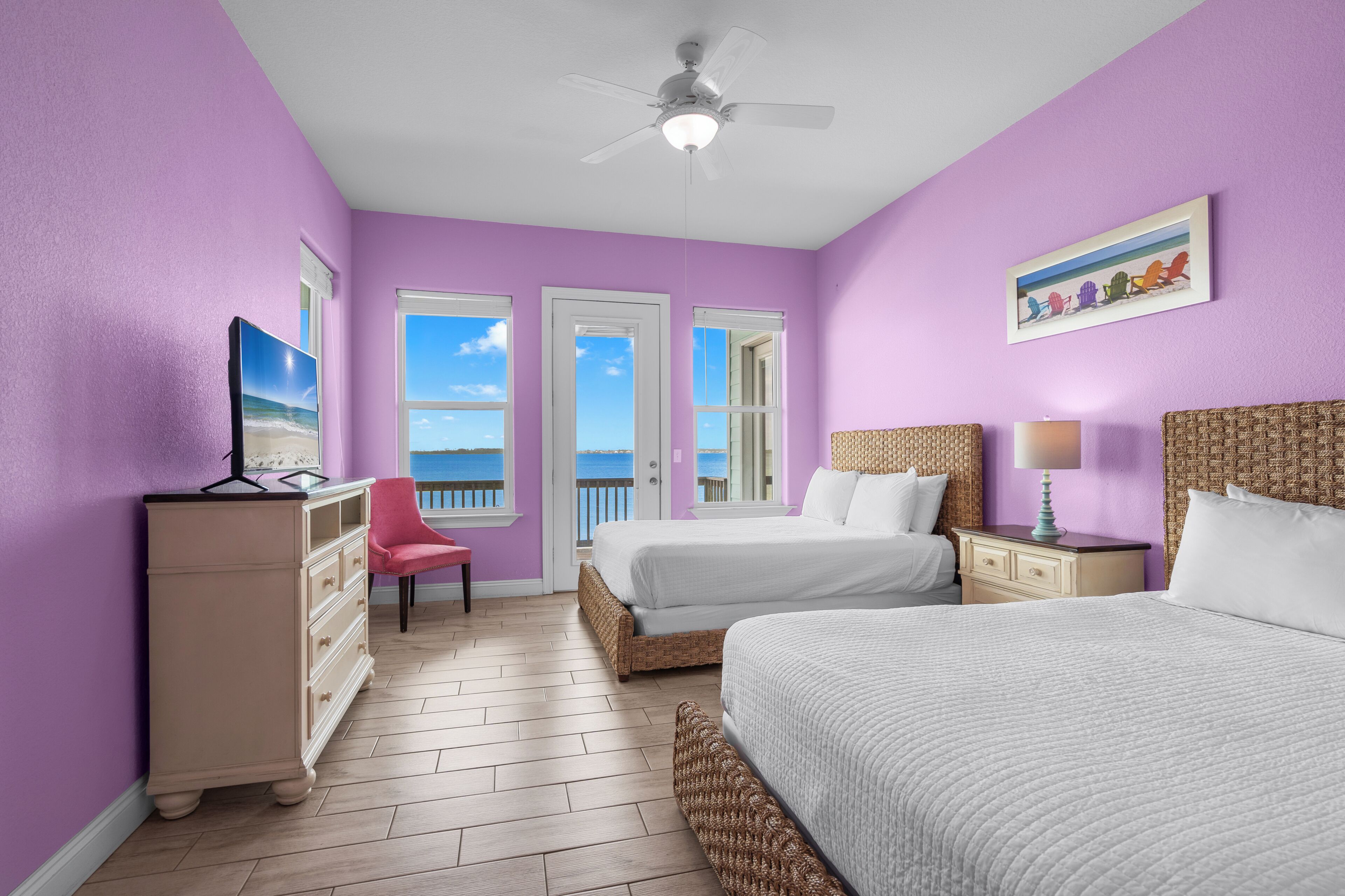 A bedroom with two beds, a dresser, a chair, a ceiling fan, and a view of the sea.