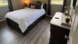 A bedroom with a bed, bedside table, lamp, and windows.