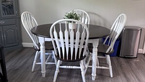 A dining table with four white chairs, a potted plant, and a trash can.