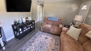 A living room with a flat-screen TV, two sofas, a coffee table, a rug, and a side table with a lamp.