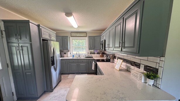 A kitchen with grey cabinets, a marble countertop, and a farmhouse sign.