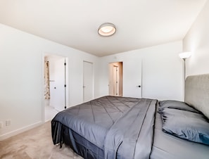 Quarto com cama, luminária no teto e porta que dá para outro cômodo.