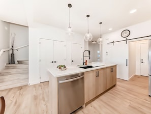Cozinha moderna com ilha central, luminárias pendentes e escada que dá acesso a um andar superior.