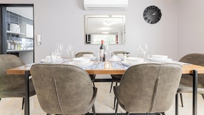 A dining area with a wooden table, grey upholstered chairs, a wall-mounted clock, and a mirror reflecting the room. - Large Hidden Gem in Poblado with A/C and gym. Steps from Provenza / Lleras. (Medellín)