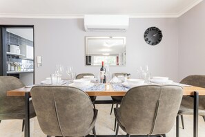 A dining area with a wooden table, grey upholstered chairs, a wall-mounted clock, and a mirror reflecting the room. - Large Hidden Gem in Poblado with A/C and gym. Steps from Provenza / Lleras. (Medellín)