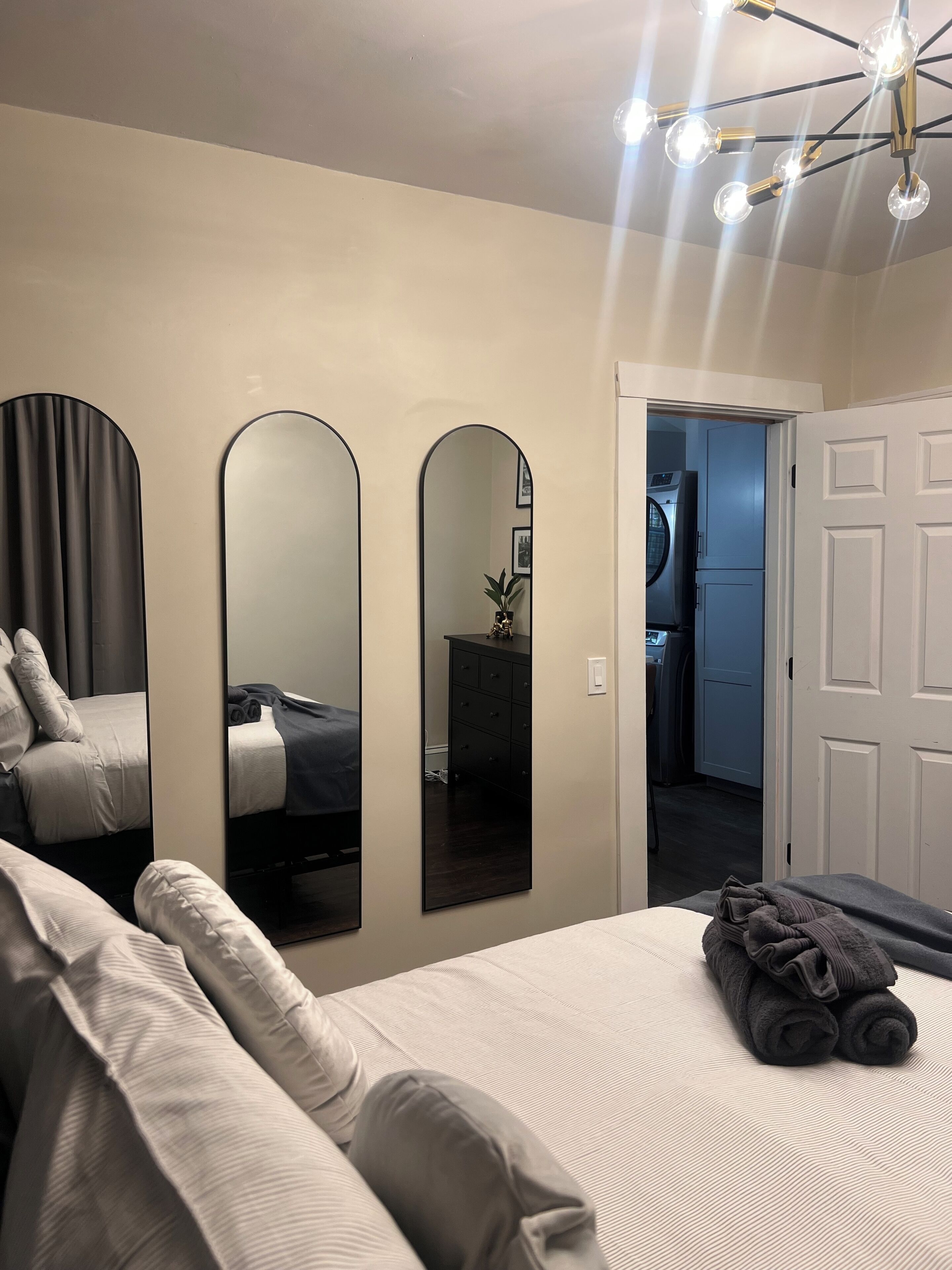 Una camera da letto con un letto, tre specchi, un lampadario e una porta che dà su un bagno.