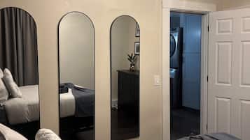 Una camera da letto con un letto, tre specchi, un lampadario e una porta che dà su un bagno.