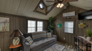 Una habitación acogedora con techo de madera, ventilador de techo, un ventanal grande, sofá, mesa y televisor.