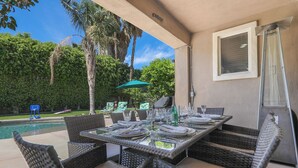 Un área de comedor exterior con mobiliario de mimbre, una piscina y vistas al jardín trasero.