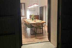 A dining area with a wooden table and chairs, a chandelier, and a view into another room.