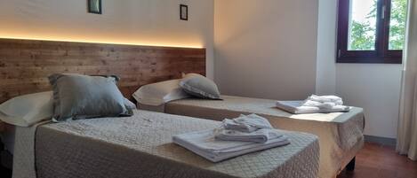 A room with two beds, each with a pillow and a folded towel on the side.