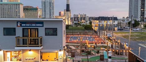 A building with a sign for mini golf and bike rentals, a deck with string lights, and a view of the city skyline.