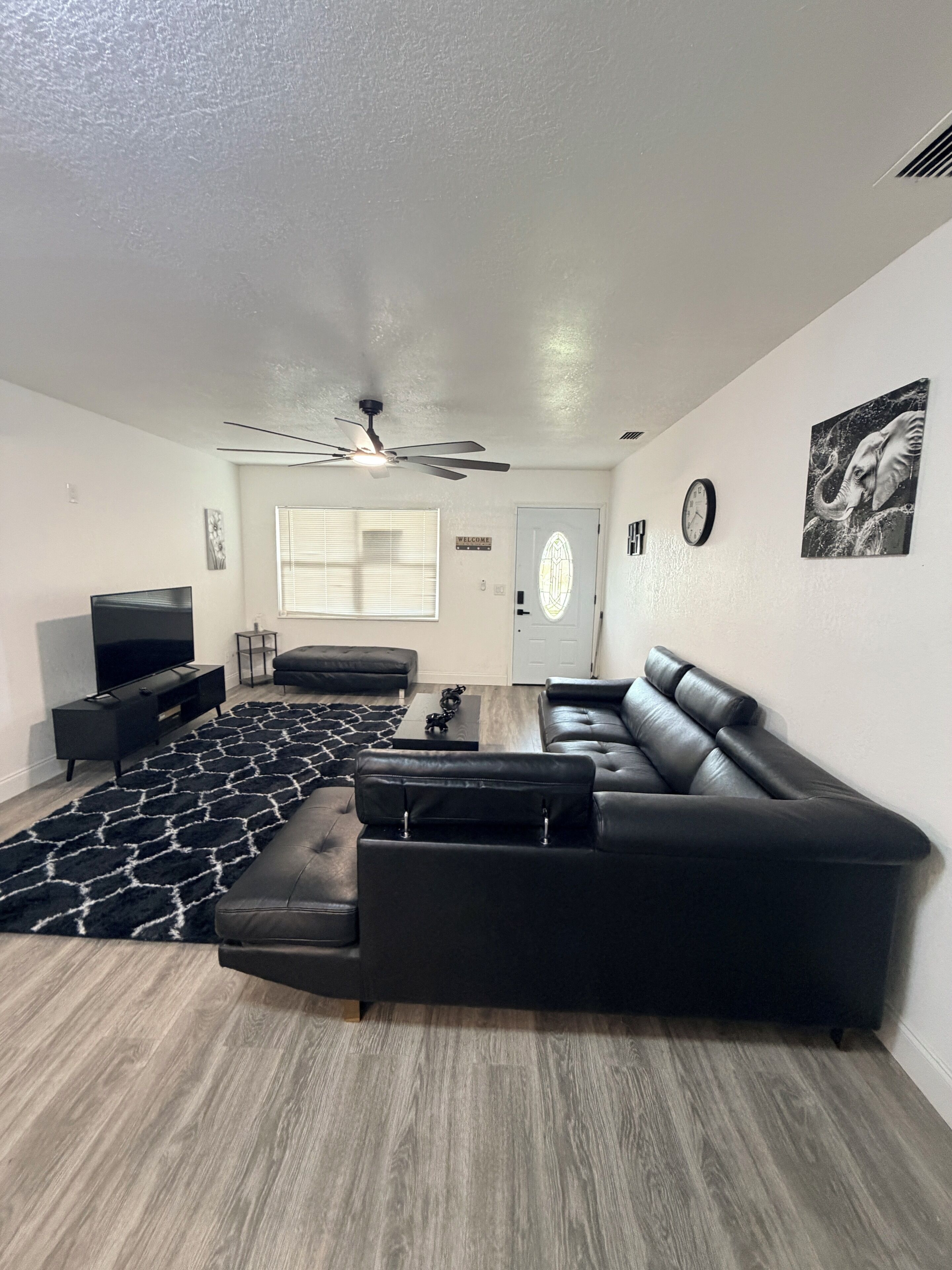 Ett modernt vardagsrum med en hörnsoffa, en platt-TV, en takfläkt och en mönstrad matta.