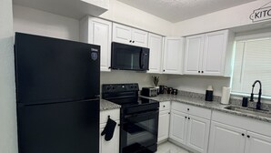 Une cuisine moderne avec des meubles blancs, un réfrigérateur noir, un four à micro-ondes, une cuisinière et un évier.