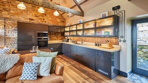 A modern kitchen with a stone wall, wooden beams, and a built-in island with a sink and countertop. - Host Stay Kingbridge Forge (Brampton)