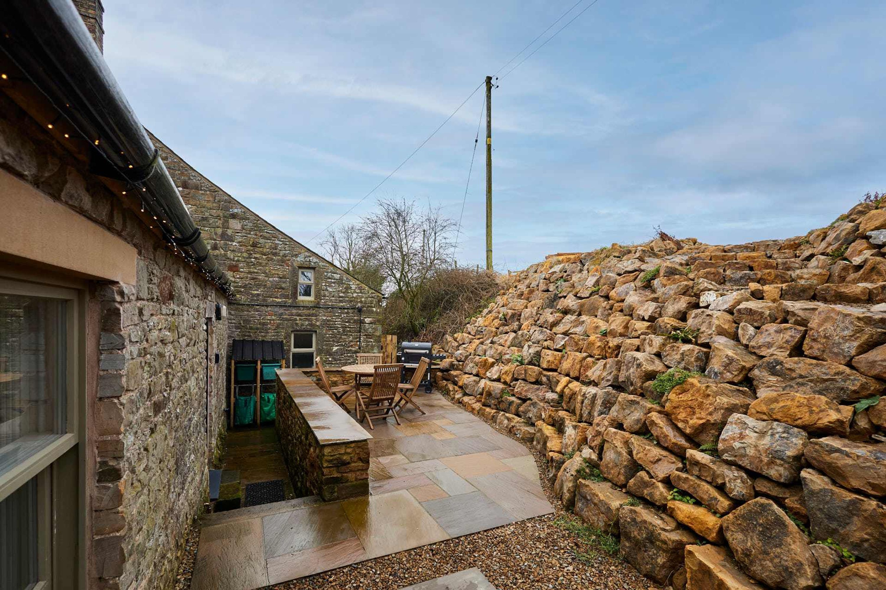 Un bâtiment en pierre doté d’une terrasse, de sièges extérieurs et d’un mur en pierre.