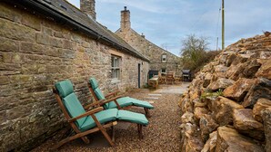 A stone building with a gravel patio, two wooden lounge chairs, and a stone wall. - Host Stay Kingbridge Forge (Brampton)