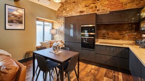 A modern kitchen with a stone wall, a dining area with a leather couch, and a framed picture on the wall. - Host Stay Kingbridge Forge (Brampton)