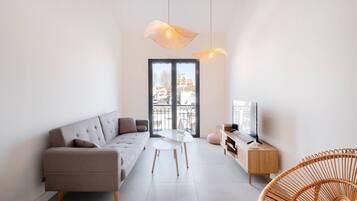 Un salon moderne avec un canapé, une table à manger, un téléviseur et un fauteuil en osier.