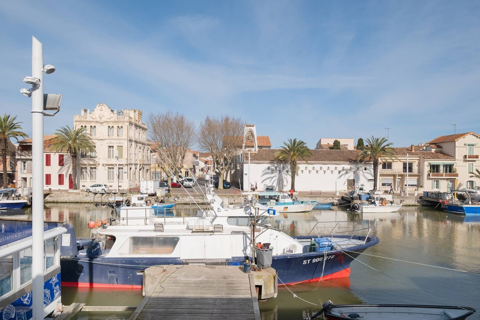 Un port de plaisance avec des bateaux amarrés, un bâtiment à l’architecture classique et un ciel dégagé.