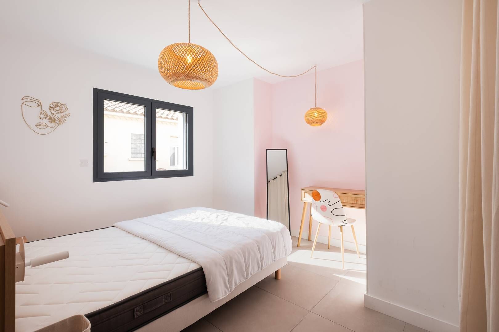 Une chambre à coucher comprenant un lit, un bureau, une chaise, un miroir et deux lampes suspendues.