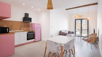 Une cuisine moderne avec un réfrigérateur rose, une table à manger et des chaises blanches, un plafond en bois et une vue à travers une porte vitrée.