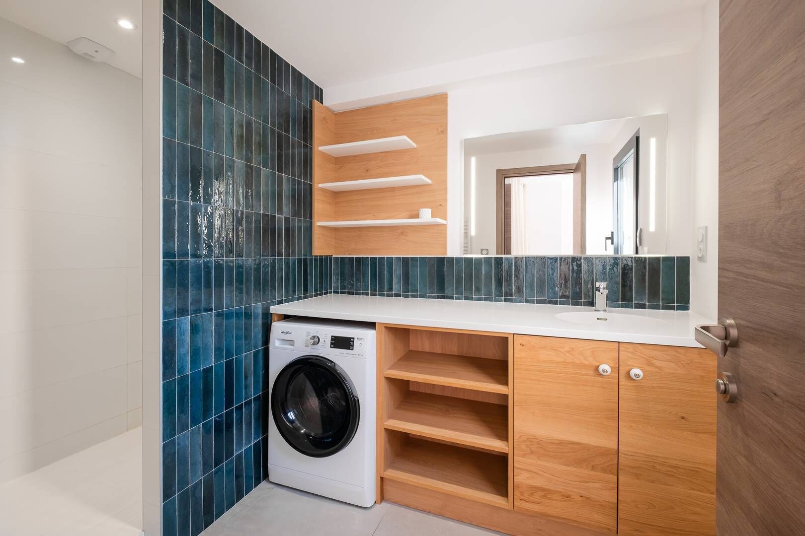 A modern bathroom with a built-in washer, wooden cabinetry, and a large mirror.