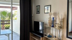Quarto com cama, escrivaninha com televisão, estante e janela com cortina.