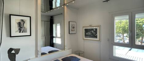 A bedroom with a bed, a mirror, a small table, and artwork on the walls.