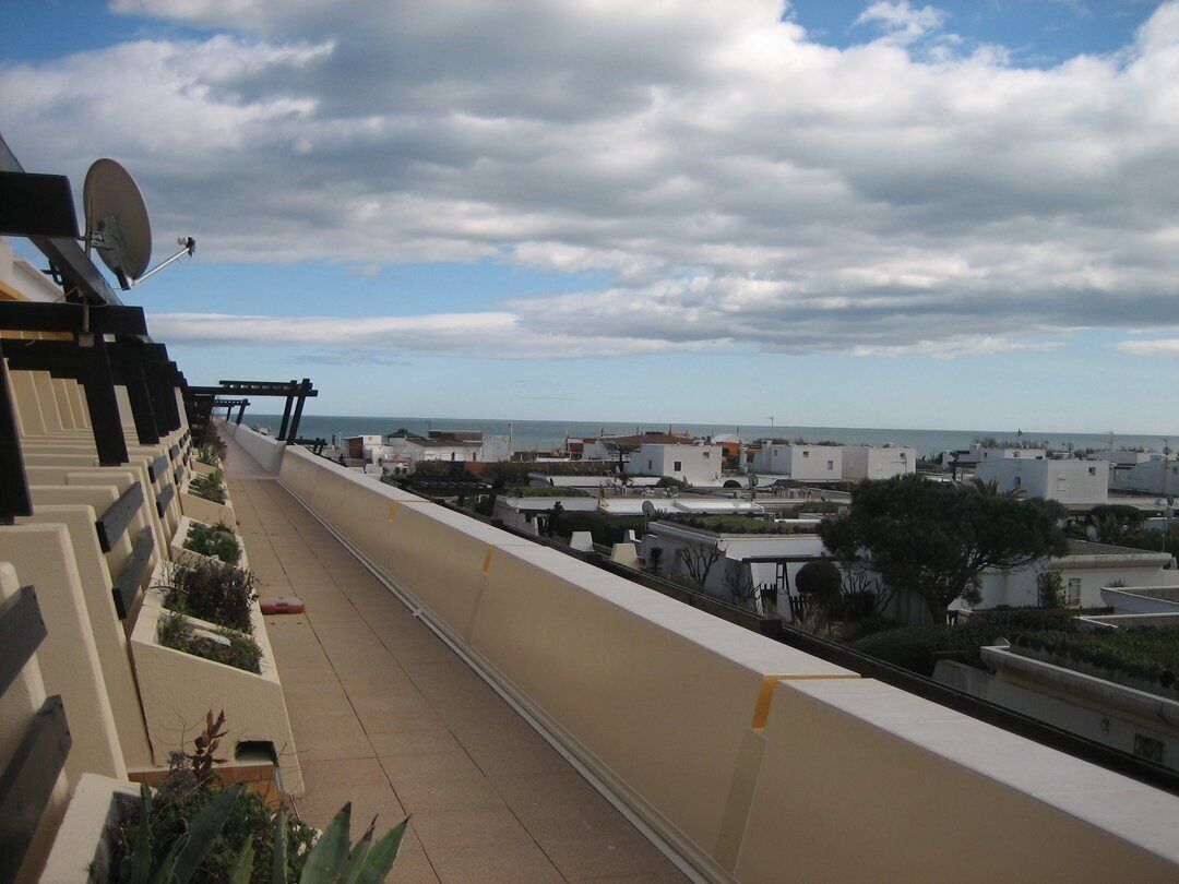 En balkon med udsigt over en kystby, en parabolantenne og en klar himmel.
