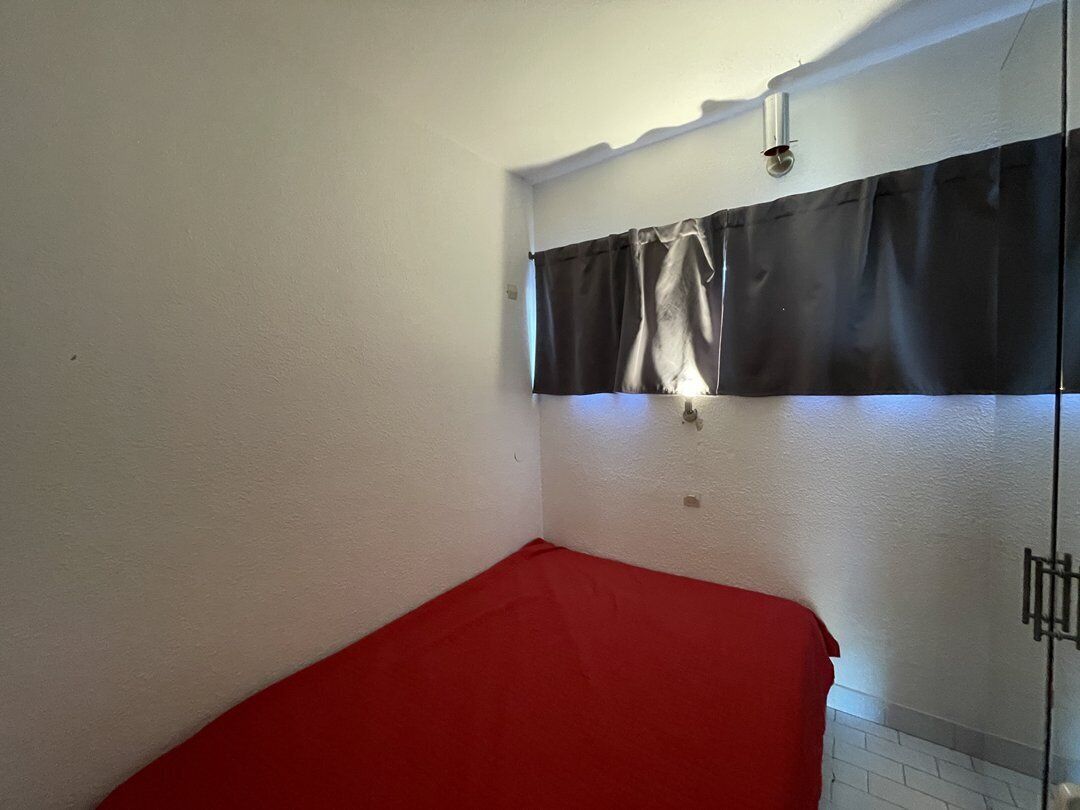 A room with a red bed, white walls, a black curtain, and a light fixture.