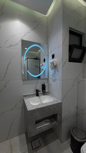 Een badkamer met een marmeren wastafel, een spiegel met blauw licht, een haardroger en een prullenbak.