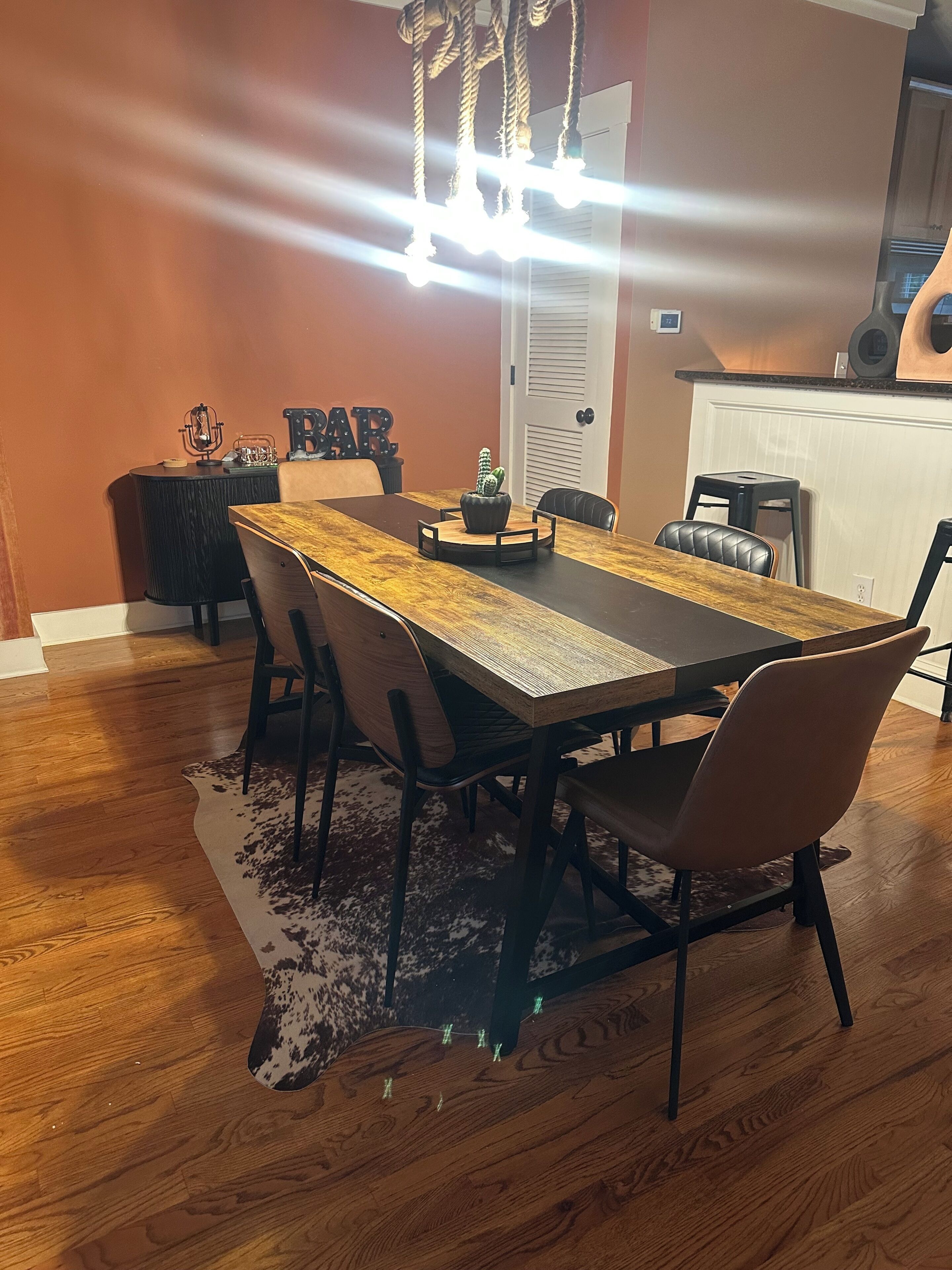 A dining area with a wooden table, chairs, a chandelier, and a cactus centerpiece.