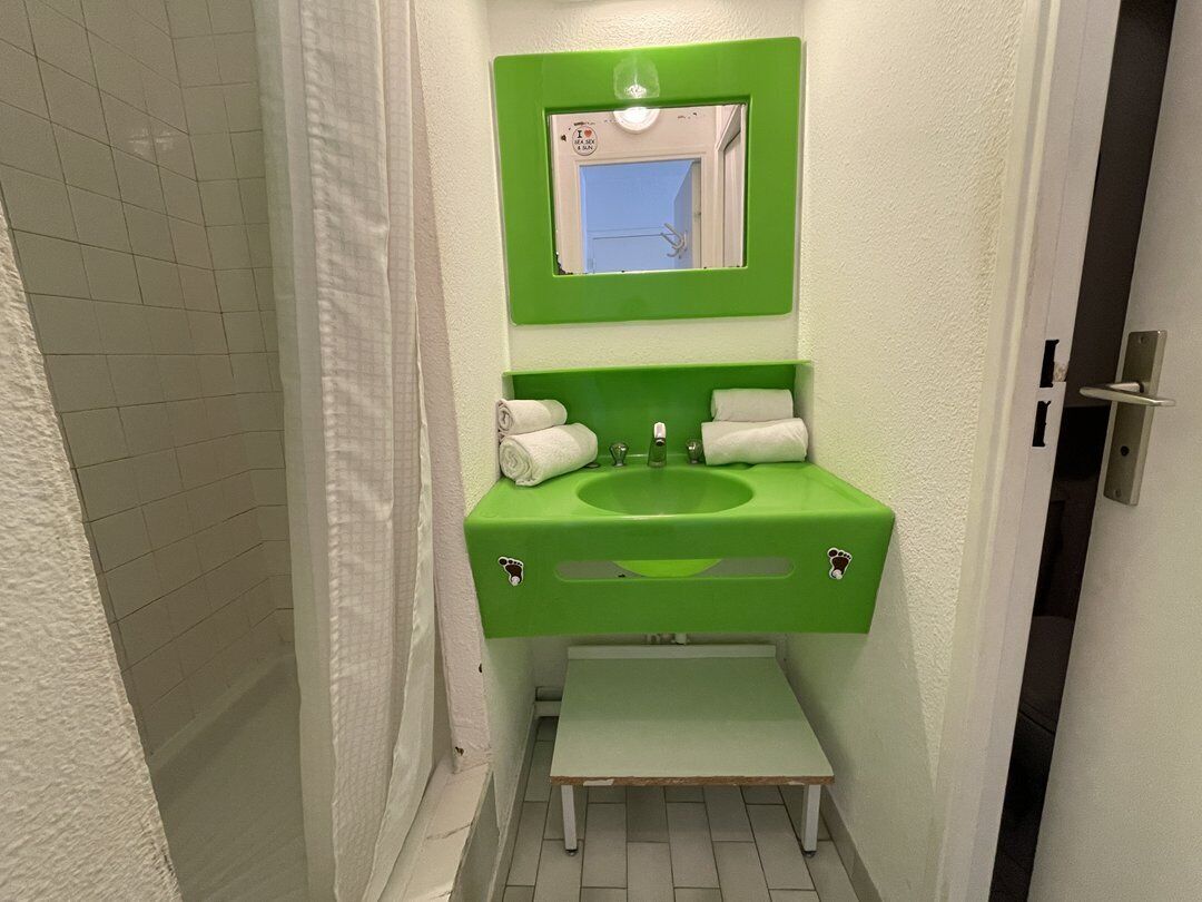 A bathroom with a green sink, white tiles, a mirror, and a small step.