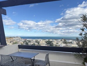 Ein Balkon mit Tisch und Stühlen mit Blick auf eine Küstenstadt, Gebäude und das Meer.