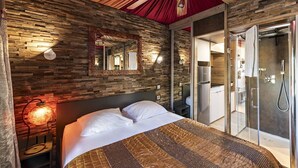 Ein modernes Schlafzimmer mit Steinwand, einem großen Bett, einem Deckenventilator und einer Duschkabine aus Glas.