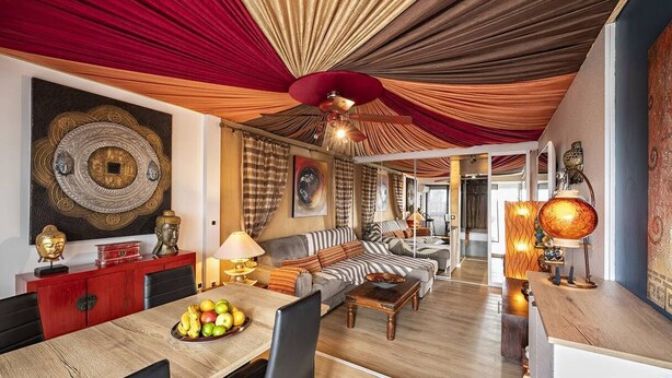 Ein großzügiger Wohnbereich mit Esstisch, Sofas und einer roten, drapierten Decke.