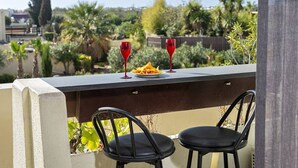 Ein Balkon mit zwei Stühlen, einem Tisch und zwei roten Gläsern.