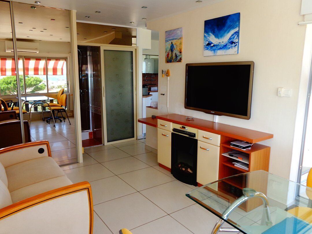 A modern living room with a glass coffee table, a flat-screen TV, and a dining area with chairs and a table.