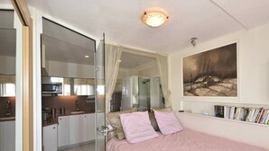 Une chambre à coucher avec un lit, une table de chevet, un miroir, un tableau accroché au mur et une bibliothèque.
