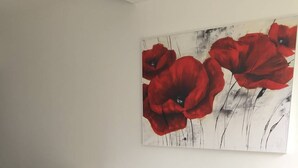 A black leather sofa with red cushions, a wooden shelf, and a painting of red flowers on the wall. - POPPY - Port Nature Studio 461 - Luxury - 2 people (AGDE)